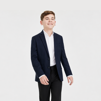 Young boy wearing a navy blazer over a white shirt and black pants on a light gray background