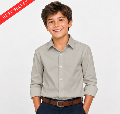 A smiling young boy wearing a light gray long-sleeve button-down dress shirt, dark navy pants, and a brown belt, standing against a light gray background. A red diagonal 'BEST SELLER' banner is visible in the top-left corner.