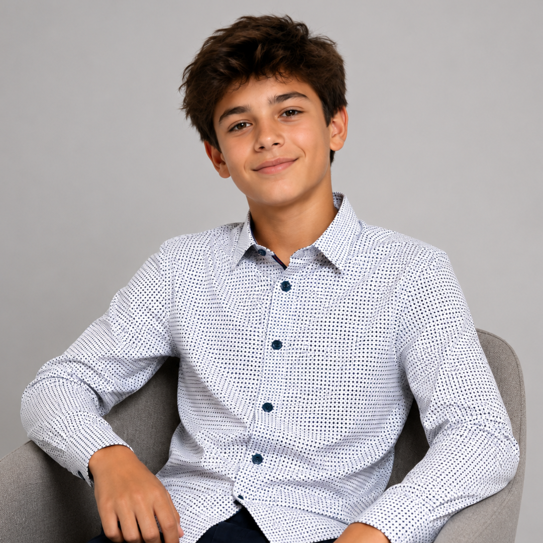 Young boy wearing a patterned shirt sitting on a gray chair against a gray background
