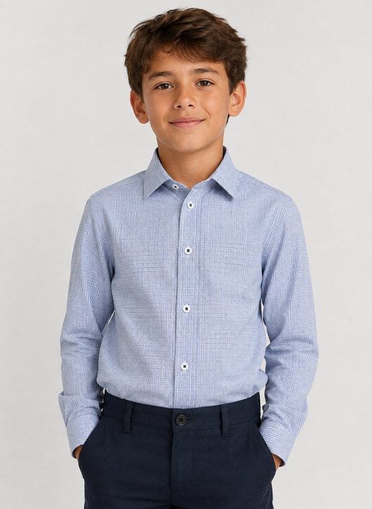 A young boy wearing a light blue and white micro-checkered long-sleeve button-down shirt with dark navy trousers, standing against a light gray studio background.