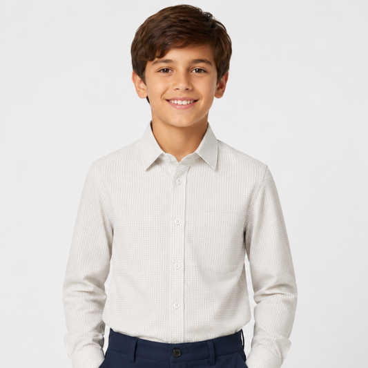 A young boy smiling, wearing a light beige textured long-sleeve button-down shirt and navy blue pants, photographed against a clean white studio background.