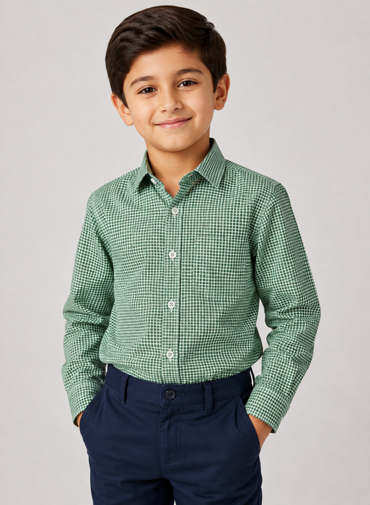 A young boy wearing a green and white micro-check patterned long-sleeve button-down shirt and navy blue trousers, standing against a light gray studio background.
