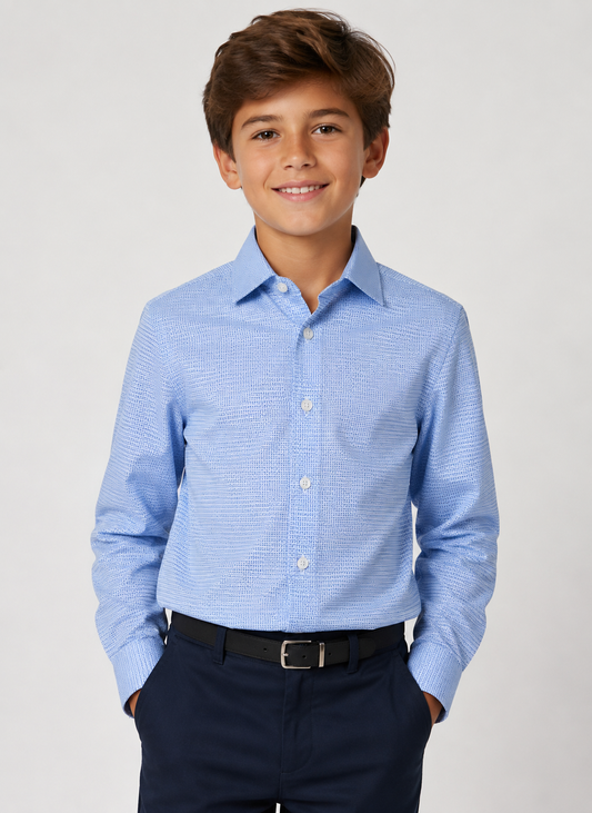 A young boy smiling, wearing a light blue long-sleeve button-down shirt with a subtle textured pattern, paired with navy pants and a black belt, against a light gray studio background.