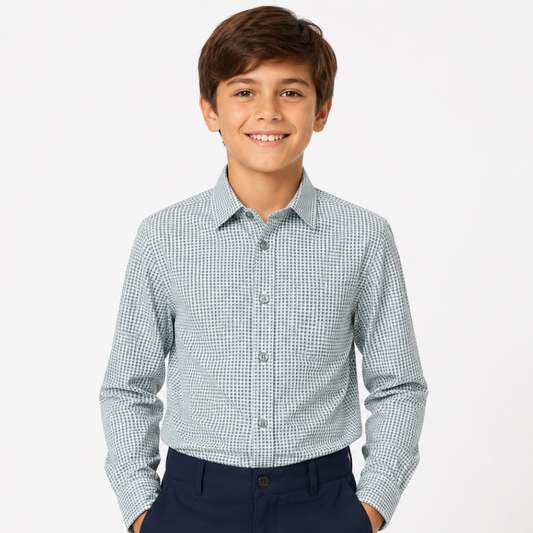 A young boy smiling, wearing a long-sleeve button-down shirt with a fine green and white micro-check pattern, paired with navy blue pants, against a solid light gray background.