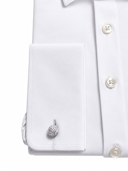Close-up of a white dress shirt cuff with a silver-toned knotted cord cufflink, shown on a white background.
