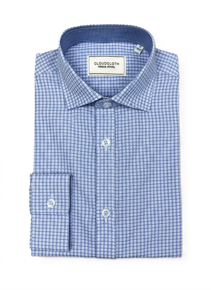 A folded men's dress shirt by Cloudcloth, featuring a blue and white micro-check pattern, a classic collar, and a button-down front.